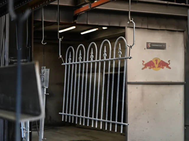 Verzinkt sierhekwerk hangt in de spuitcabine, klaar om gecoat te worden
